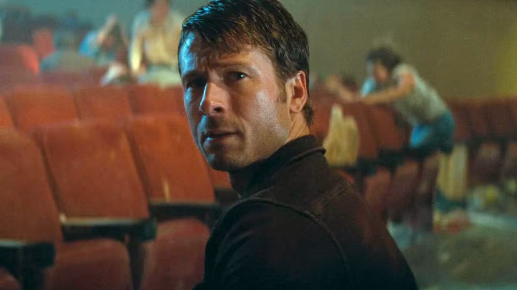 Glen Powell looking back over his shoulder in a theater in Twisters