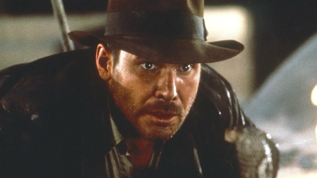 A man in a fedora looks scared facing a snake