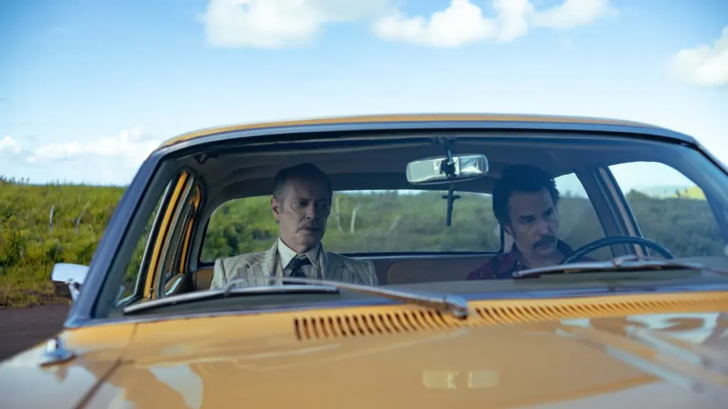 Steve Buscemi dan Sam Rockwell duduk bersama di mobil kuning cerah di Pulau Paskah dalam film komedi hitam WILD HORSE NINE.